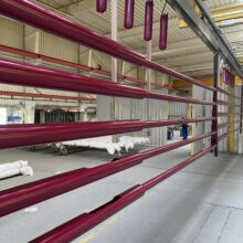 Hier sind die frisch pulverbeschichteten Maste in der Farbe Bordeauxviolett zu sehen. Diese Maste sind zylindrisch abgesetzt produziert, was an den zwei verschiedenen Rohrdurchmessern zu sehen ist. Die Duplex-Beschichtung, hier am Beispiel der Pulverbeschichtung nach DIN 55633, eine Kombination aus Feuerverzinkung und anschließender farblicher Beschichtung, wird aus Gestaltungsgründen farblicher Art oder aus Schutzgründen des Mastes gewählt oder auch aus einer Kombination aus beidem. Ein Duplexverfahren verlängert zudem die Schutzdauer weitaus mehr als die Summe der beiden einzelnen Verfahren, da der Zink vor chemischen und atmosphärischen Umwelteinflüssen langfristig geschützt wird.