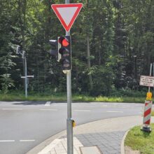 Ein Standmast wiederum trägt eine Lichtsignalanlage für die Fahrzeuge, die unmittelbar vor der Ampelanlage stehen. Im vorliegenden Fall dient der Standmast für die Lichtsignalanlage für den Autoverkehr, der Fußgänger als auch für den Taster für die Fußgänger, um der Leitzentrale zu melden, dass ein Fußgänger die Straße überqueren möchte.